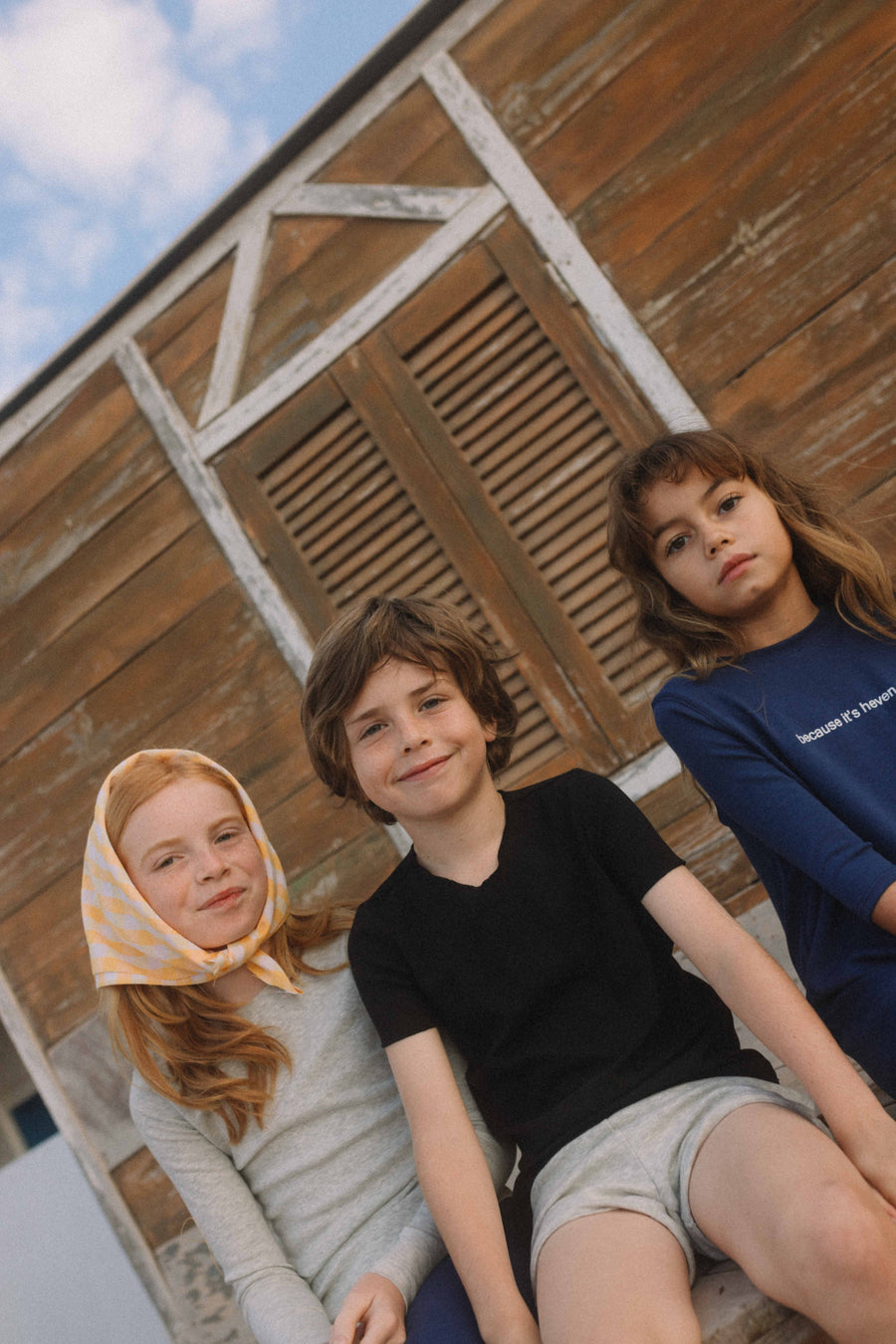8 year old boy wearing black tee and grey track shorts sitting with two little girls