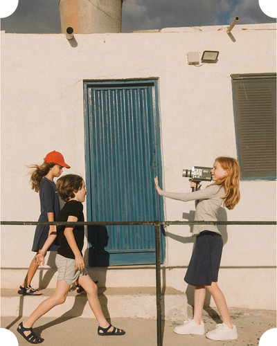 Young boy and girl walking towards a young girl using an old fashioned video camera