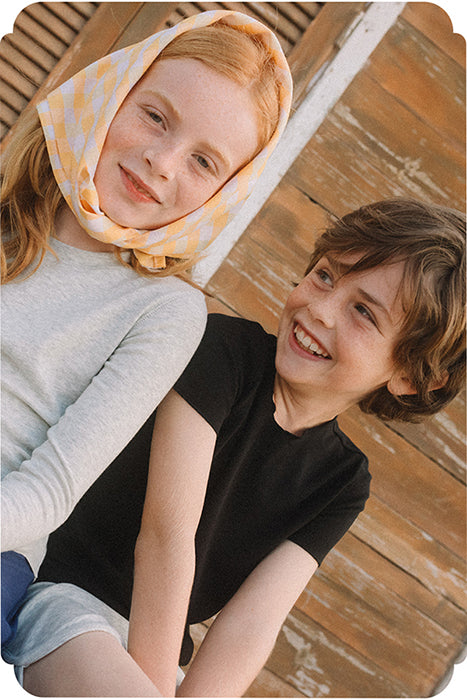 young girl wearing a long sleeve tee sitting next to a boy wearing short and a black short sleeve tee