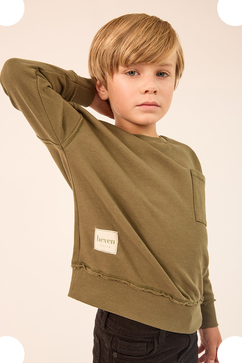 Young boy facing sideways wearing a olive sweatshirt and pants