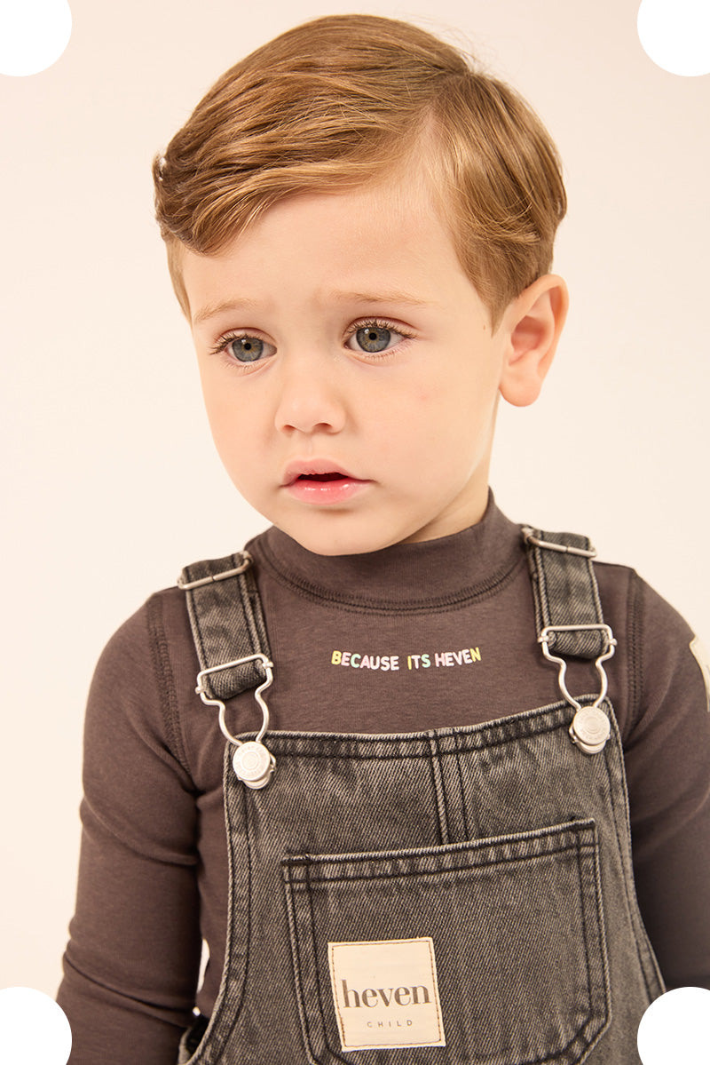 A toddler wearing denim overalls and long sleeve tee.