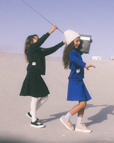 Two girls wearing Heven sweatshirts and skirts One in all blue and one wearing all black.