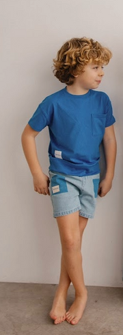 Child wearing a blue t-shirt and denim shorts against a plain background