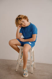 Child sitting on a stool wearing a blue outfit against a plain background