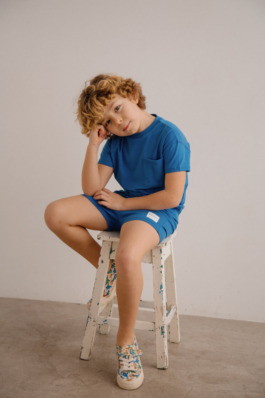 Child sitting on a stool wearing a blue outfit against a plain background