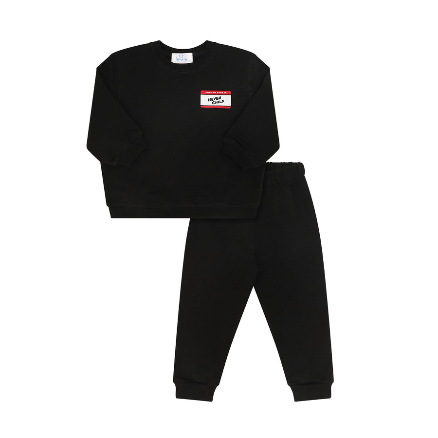 A two-piece kids' sweatshirt and jogger pants set in black. The sweatshirt features a small rectangular chest patch with a red top border, white background, and black text reading 'MONTI CROWE'.