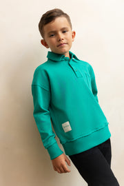 Child wearing a teal sweatshirt with a logo on a beige background