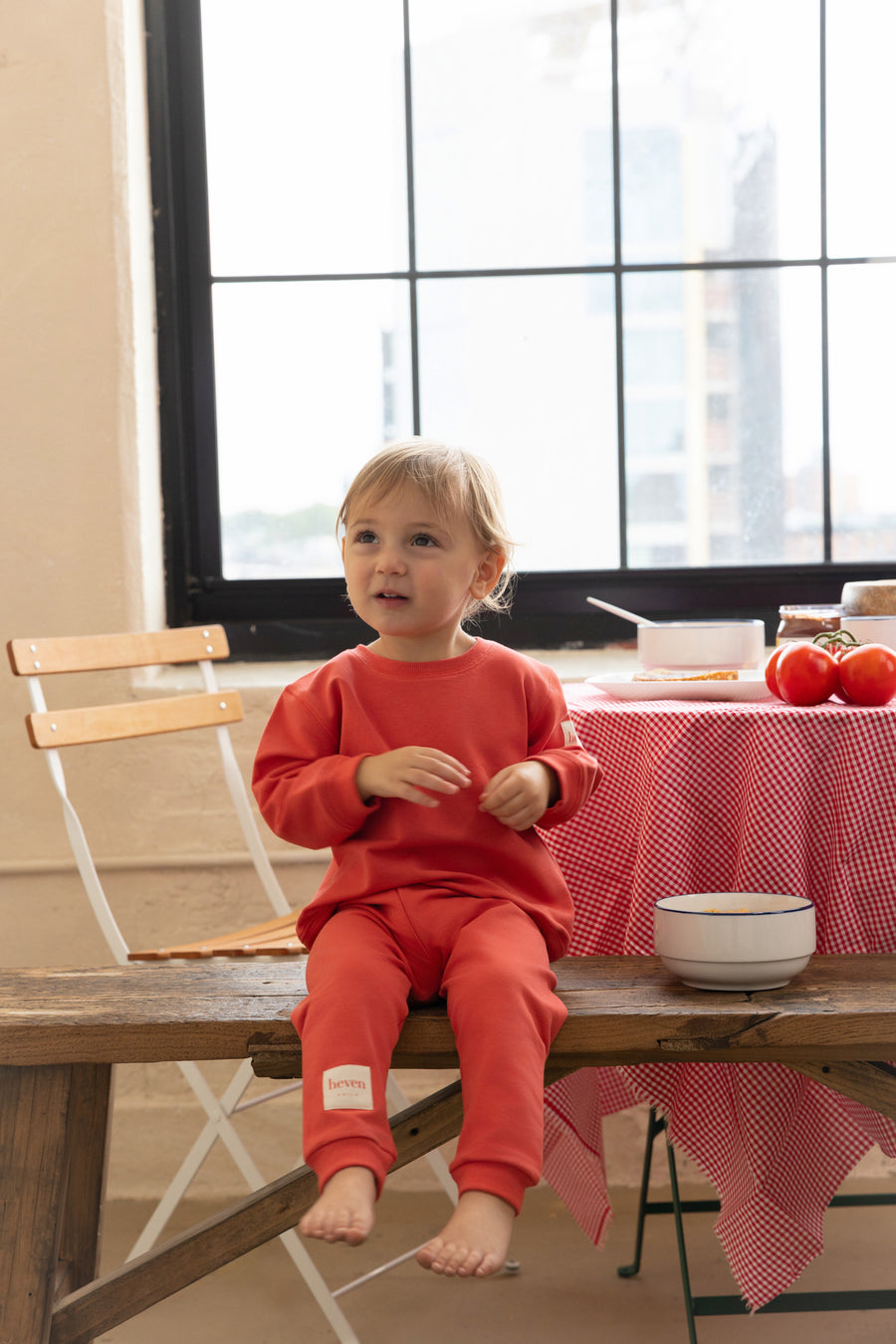 Child in red pajamas sitting on a wooden table with a checkered tablecloth.