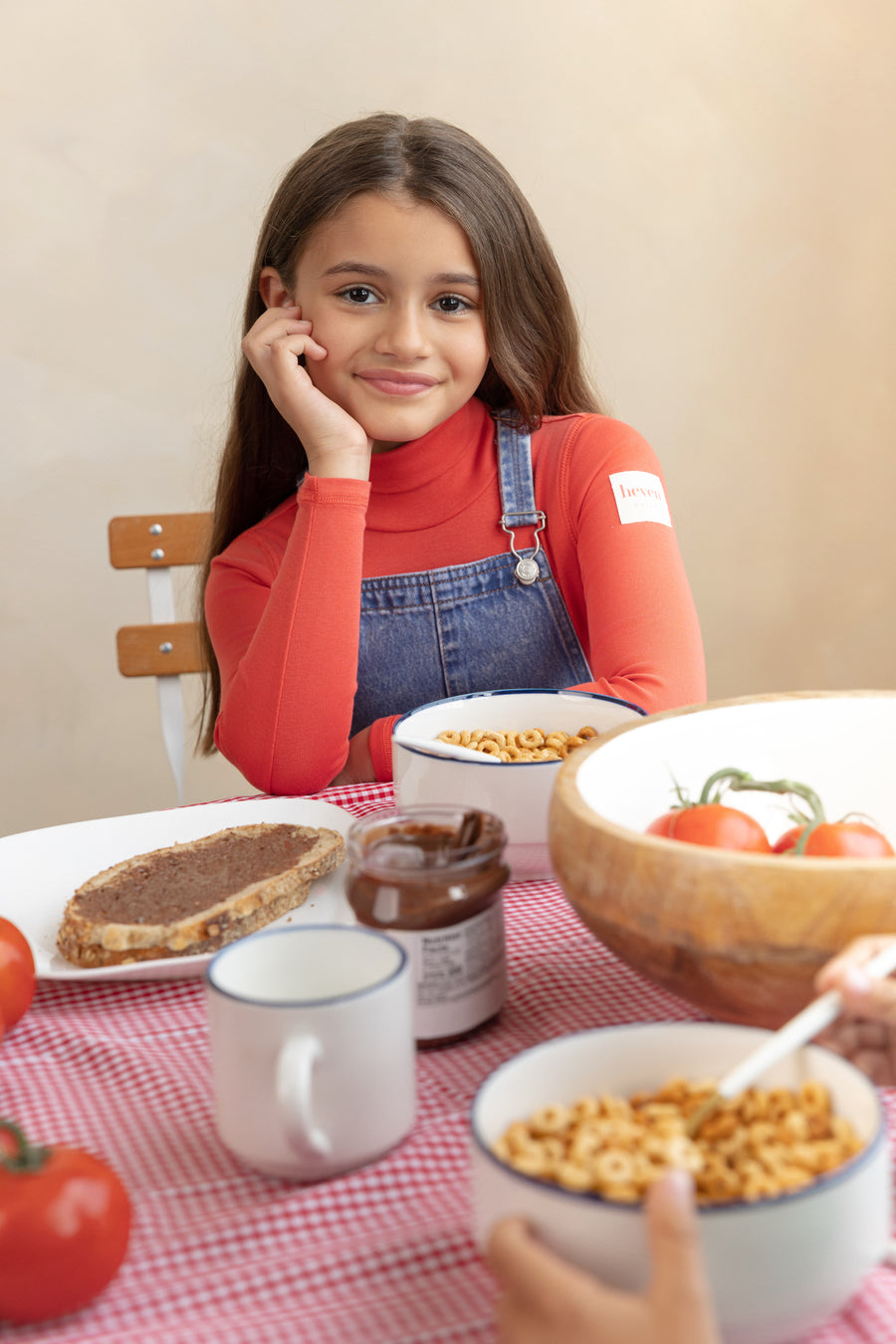 Young girl sitting at a table with food, including a bowl of cereal and a jar of peanut butter.