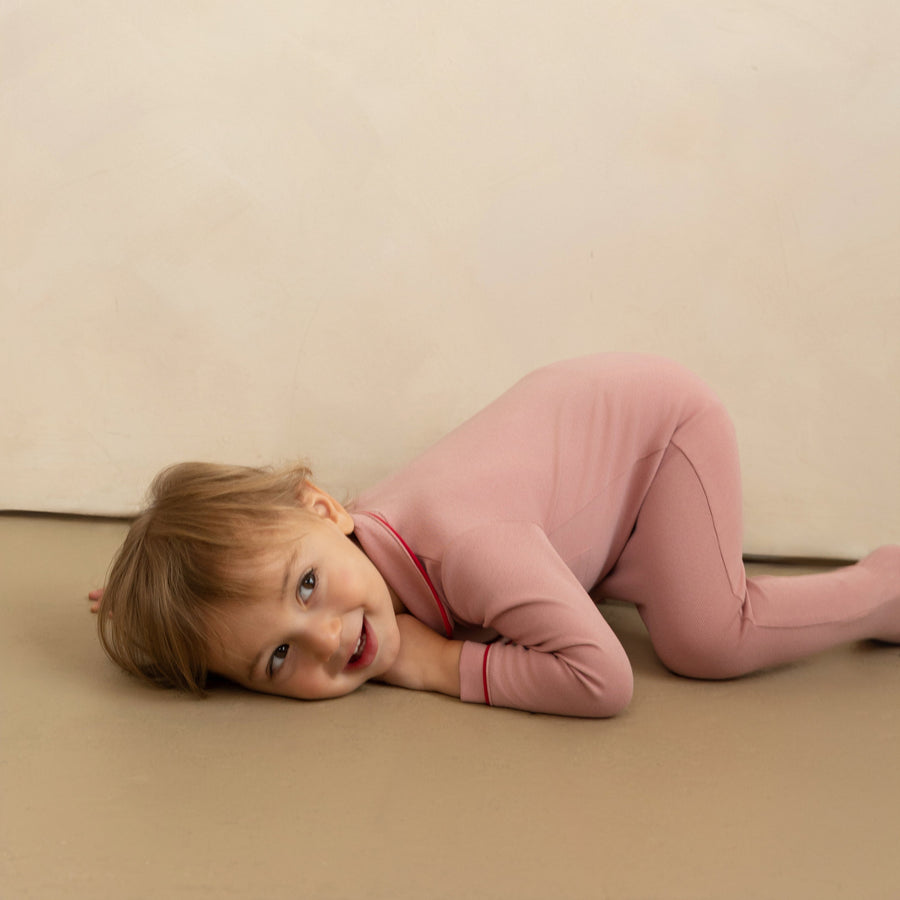 Child in pink outfit lying on a beige surface with a plain background