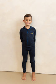 Child wearing navy blue pajamas with a logo on a beige background