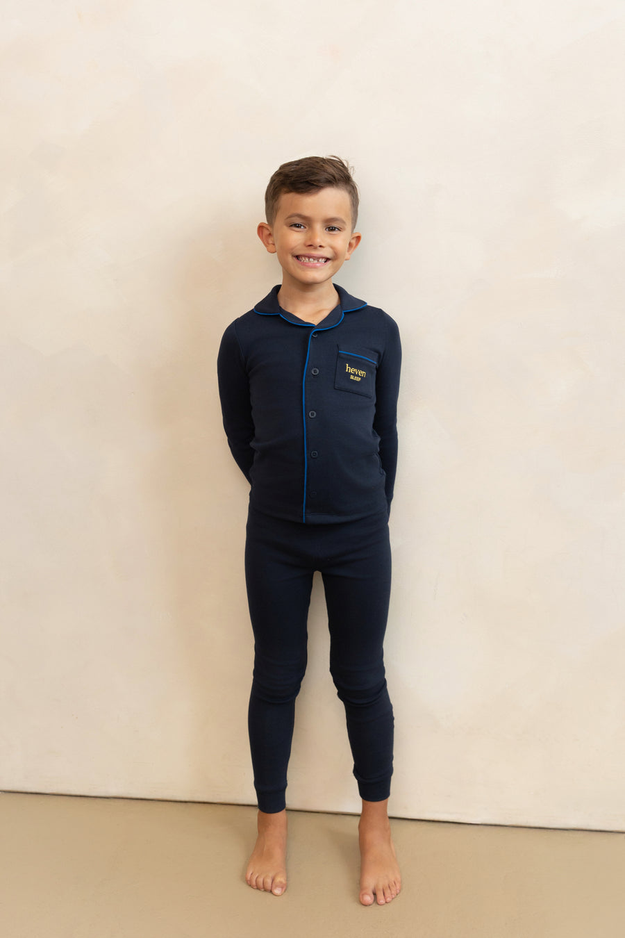 Child wearing navy blue pajamas with a logo on a beige background