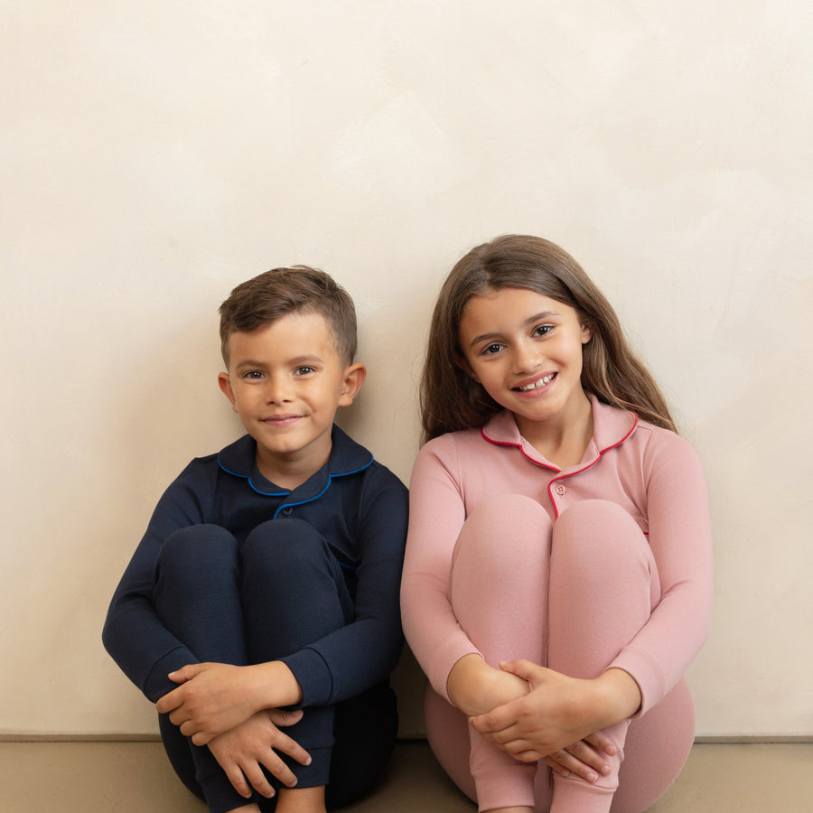 Two children in matching pajama sets sitting on the floor against a plain background