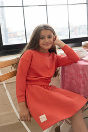 Young girl in a red dress sitting at a table with a checkered tablecloth.