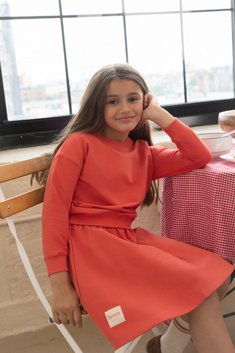 Young girl in a red dress sitting at a table with a checkered tablecloth.