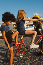boy leaning on a red bike wearing a blue and black short sleeve t-shirt