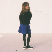 Girl wearing black sweatshirt and blue short skirt with black tights and black sneakers