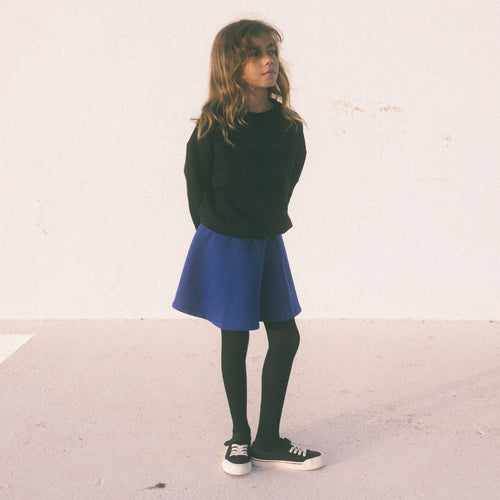 Girl wearing black sweatshirt and blue short skirt with black tights and black sneakers