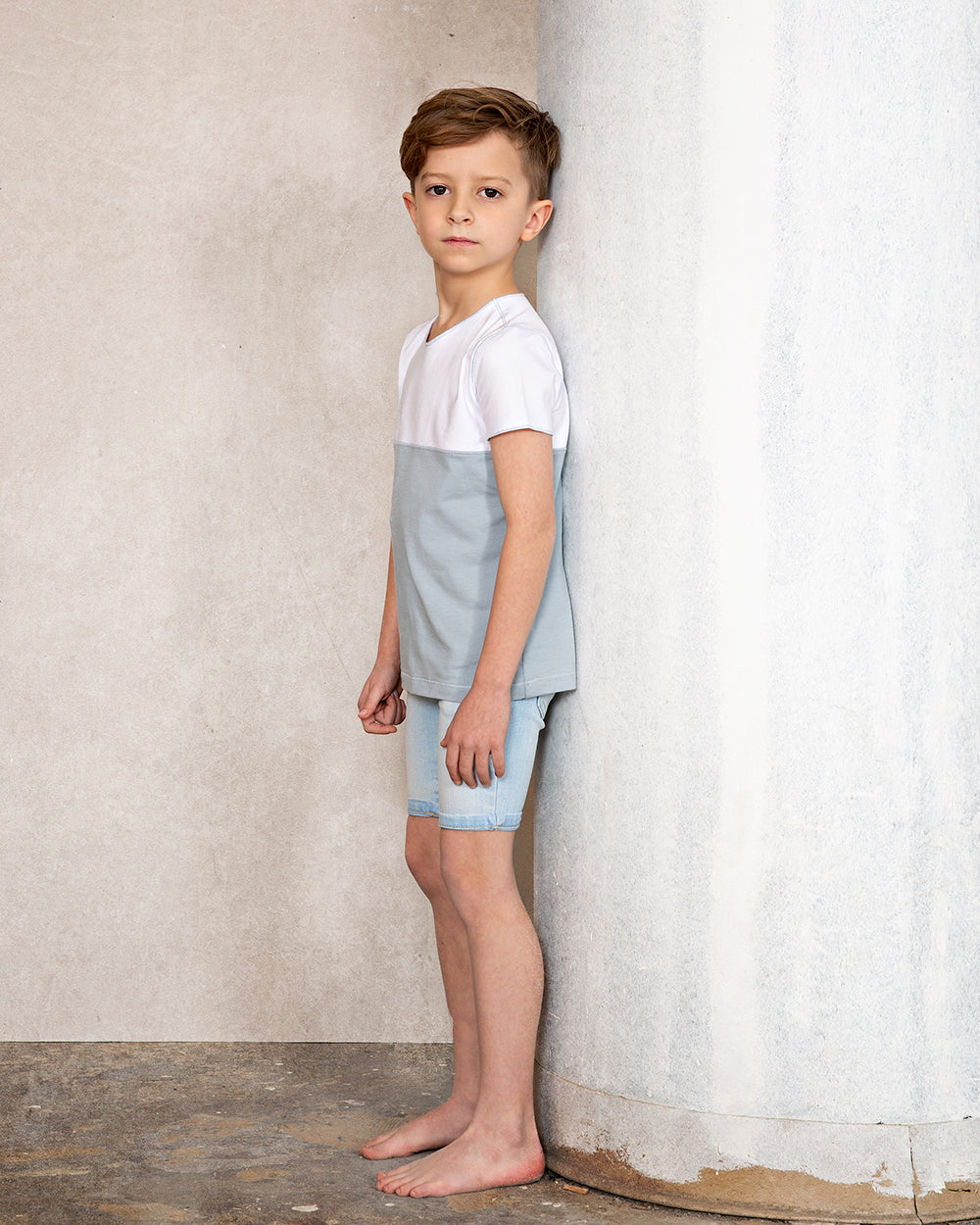 Young boy wearing short sleeve color block light blue and white color block tee and denim shorts