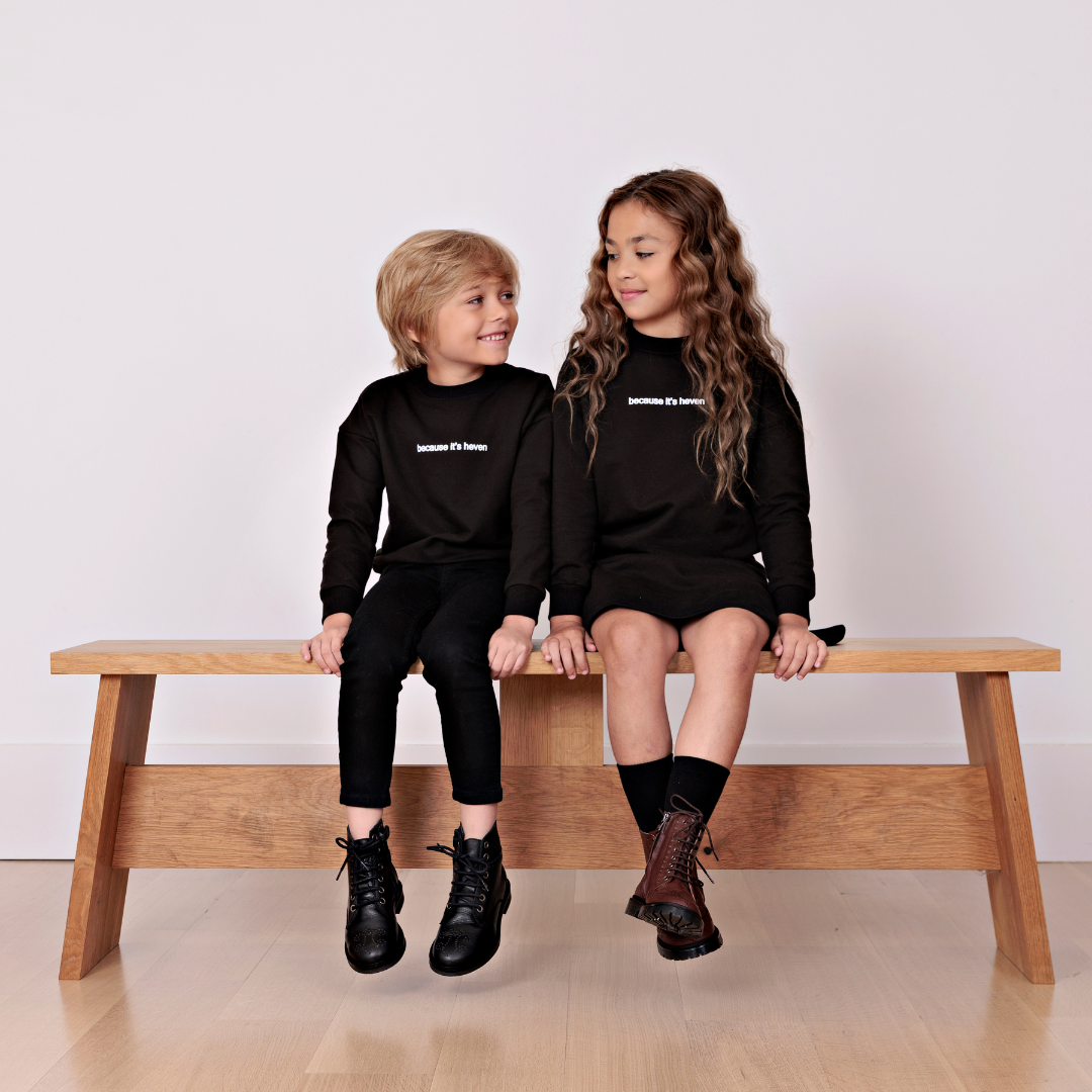 one boy and one girls sitting on a bench wearing black sweatshirts and the boy is wearing pants and the girl is wearing a matching skirt