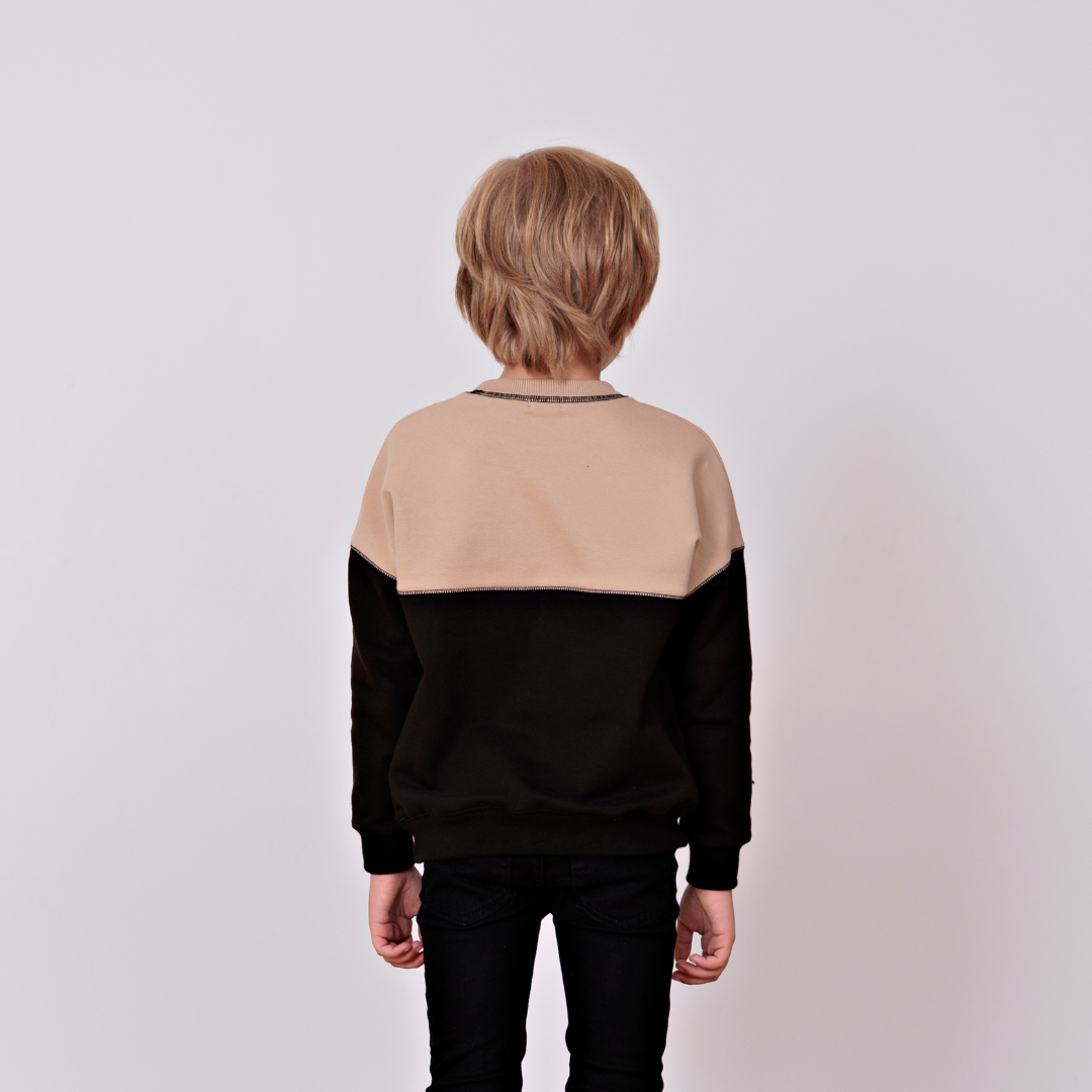 The back view of a young boy wearing a color block tan and black sweatshirt